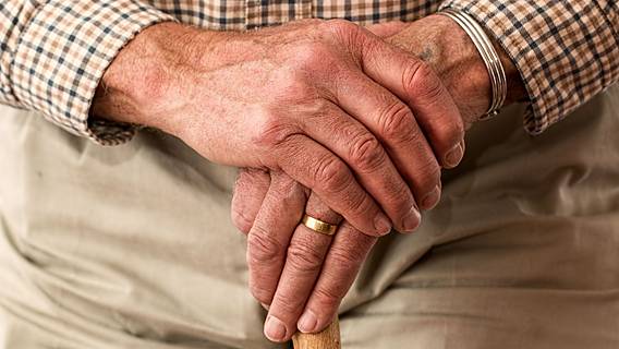 Die Hände eines alten Mannes stützen sich auf einen Gehstock.