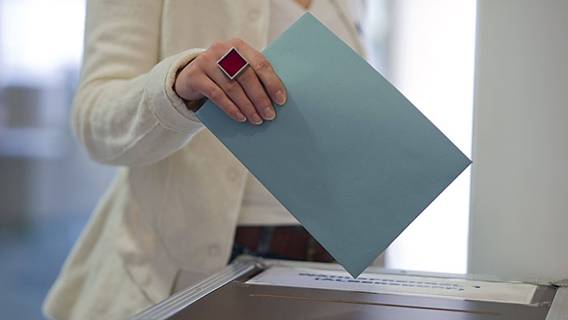 Symbolfoto: Frau wirft einen Wahlzettel in eine Wahlurne.