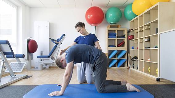 Symbolbild: Ein Mann macht Übungen in einer Physiotherapie-Praxis. Eine Physiotherapeutin leitet ihn dabei an.