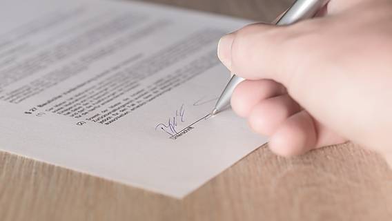 Eine Hand hält einen Stift und unterschreibt ein Dokument.