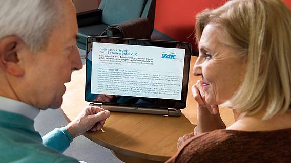 Symbolfoto: Ein älteres Paar sitzt gemeinsam vor einem Tablet-PC, auf dem Infos vom VdK zu sehen sind.
