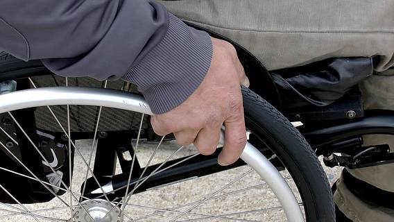 Das Bild zeigt einen Rollstuhl, auf dem Rad liegt die Hand des Fahrers.