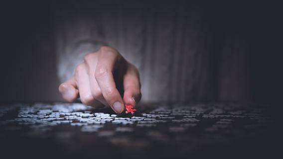 Das Bild zeigt eine hand, die ein rotes Puzzleteil in ein weißes Puzzle einfügt