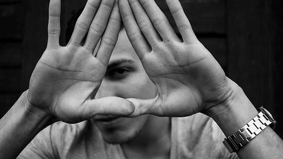 Das Foto zeigt einen jungen Mann, der seine Hände wie ein Dreieck vor sein Gesicht hält.