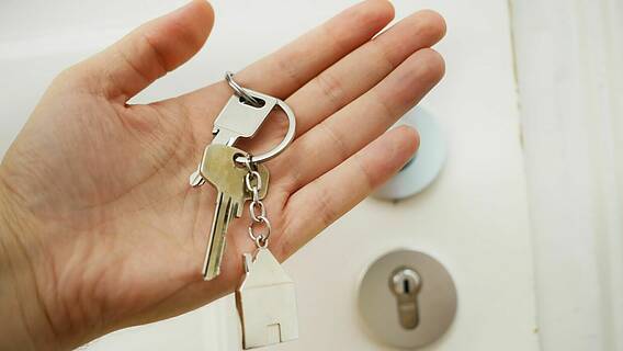 Das Bild zeigt eine Hand, die einen Schlüssel hält, im Hintergrund ist ein Ausschnitt der Haustür zu ssehen.