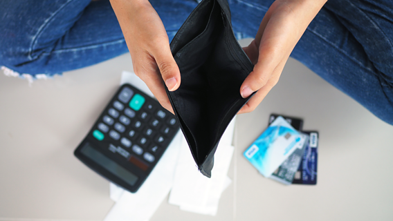 Das Bild zeigt ein leeres Portemonnaie, einen Taschenrechner und Kreditkarten
