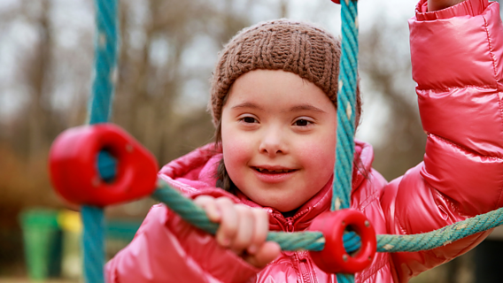 Ein Mädchen mit Down-Syndrom auf dem Spielplatz lachend.