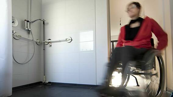 Symbolfoto: Eine Frau im Rollstuhl im Badezimmer neben einer ebenerdigen Dusche