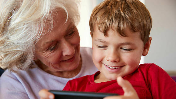Symbolfoto: Ältere Frau und kleiner Junge schauen gemeinsam lachend auf ein Smartphone