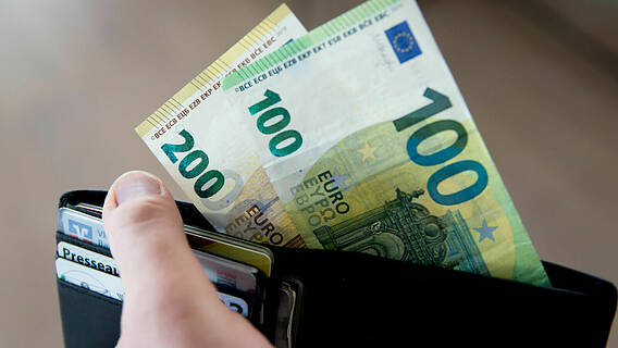 Symbolfoto: Eine Hand hält eine Geldbörse, aus dieser schauen ein 100- und ein 200-Euro-Schein heraus.