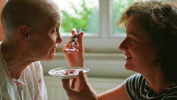 Symbolfoto: Eine jüngere Frau hilft einer älteren Frau beim Essen, füttert sie mit einem Löffel