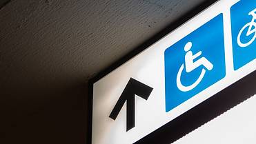 Das Bild zeigt ein Schild mit einem Pfeil und einem Rollstuhl Symbol, der den barrierfreien Zugang anzeigt
