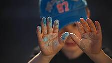 Das Foto zeigt einen kleinen Jungen, der seine farbverschmierten Hände hochhält.