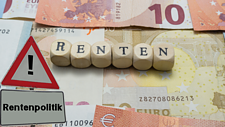 Das Symbolfoto zeigt Euroscheine, darauf Buchstabenwürfel, die das Wort "Renten" bilden, und ein Verkehrsschild mit der Aufschrift Rentenpolitik