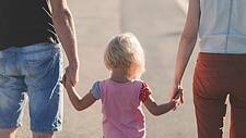Ein kleines Mädchen geht zwischen seinen Eltern, hält beide an den Händen