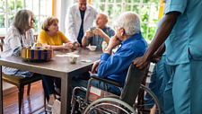 Das Bild zeigt mehrere ältere Personen udn Pflegepersonal beim Kartenspielen.