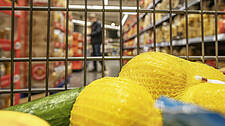 Symbolfoto: Ein Einkaufswagen mit Waren darin, im Hintergrund sieht man eine Person an einem Supermarktregal stehen