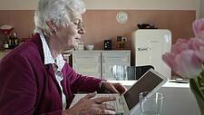 Symbolfoto: Ältere Frau sitzt in ihrer Küche an einem Notebook, schaut konzentiert auf den Bildschirm