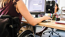 Symbolfoto: Junge Frau im Rollstuhl an ihrem Schreibtisch mit PC bei der Firma Böhringer Ingelheim