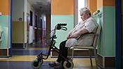 Symbolfoto: Eine Frau sitzt einsam auf dem Flur eines Pflegeheims, vor sich einen Rollator