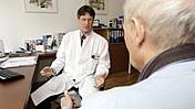 Symbolfoto: Ein Arzt und ein älterer Patient im Sprechzimmer, sie unterhalten sich.