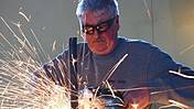 Symbolfoto: Ein älterer Arbeitnehmer arbeitet mit einer Funken sprühenden Metall-Flex