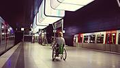 Symbolfoto: Eine Frau im Rollszuhl an einem Bahnsteig in Hamburg. Auf den Gleisen links und rechts von ihr ihr stehen Züge.