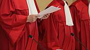 Symbolfoto: Richter des Bundesverfassungsgerichtes in roten Roben, einer hält Dokumente in der Hand