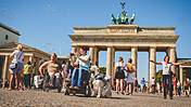 Symbolfoto: Der Pariser Platz vor dem Brandenburger Tor in Berlin. Viele Menschen mit und ohne Rollstuhl halten sich dort auf, machen Fotos.