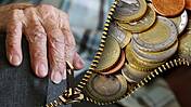 Symbolfoto: Die Hand einer alten Person. Das Bild wird von einem Reißverschluss geteilt, durch dessen Öffnung Euromünzen zu sehen sind.
