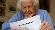 Symbolfoto: Eine ältere Frau hält nachdenklich ein Dokument in der Hand, auf dem "Rentenbescheid" steht.