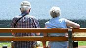 Zwei Rentner sitzen in der Sonne auf einer Bank.