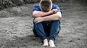 Symbolfoto: Ein Junge sitzt auf dem Boden, den Kopf in den verschränkten Armen verborgen. Das Bild wirkt traurig und trostlos.