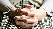 Eine alte Frau hält ihre gefalteten Hände auf ihren Knien.