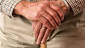 Ein Alter Mann stützt seine Hände auf einen Stock.