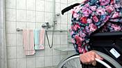 Eine alte Frau im Rollstuhl fährt aus ihrem barrierefreien Badezimmer.
