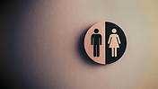 Das Foto zeigt ein rundes Schild, auf dem ein Piktogramm für "Mann" und eins für "Frau" nebenander abgebildet sind.
