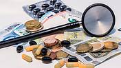 Das Foto zeigt ein Stethoskop, Pillen und daneben Geldscheine und Münzen