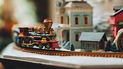 Eine historische Miniatur-Eisenbahn auf Schienen vor kleinen Häuschen