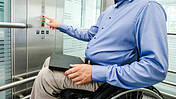 Ein Mann trägt ein Hemd, sitzt im Rollstuhl und benutzt den Aufzug