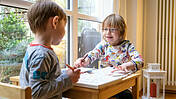 Zwei Kinder mit Behinderung sitzen gemeinsam an einem kleinen Tisch und spielen
