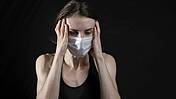 Eine Frau mit Mund-nasen-Schutz hält sich den Kopf