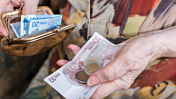 Das Bild zeigt die Hände eienr älteren Frau, die 10- und 20-Euroscheine sowie einige Münzen hält.