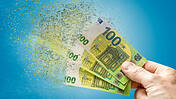 Symbolfoto: Jemand hält drei 100-Euro-Scheine in der Hand, diese zerfallen, lösen sich in Luft auf