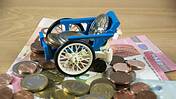 Symbolfoto: Geldscheine und Münzen, darauf steht ein Spielzeug-Rollstuhl