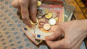 Symbolbild: Hand eines älteren Menschen vor diversen Euro-Scheinen und -Münzen.