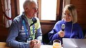 Fritz Fischer und Verena Bentele sitzen nebeneinander, sie interviewt ihn, hält ein Mikrofon in der Hand.