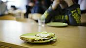 Symbolfoto zum Thema Kinderarmut und Kindergrundsicherung: Ein Tisch in einer grundschule, ein Kind sitzt und isst. Im Vordergrund ein Brot auf einem Teller.