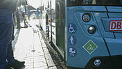 Symbolfoto: Ein Bus an einer Haltstelle, vorne sind Aufkleber angebracht mit Piktogrammen für Reisende mit Behinderung, Menschen mit Gehstock und für Kinderwagen