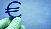 Symbolfoto: Hand im Latexhandschuh hält Eurozeichen